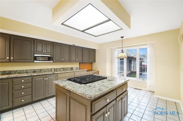 kitchen with pendant lighting, a kitchen island, light stone countertops, and dark brown cabinets