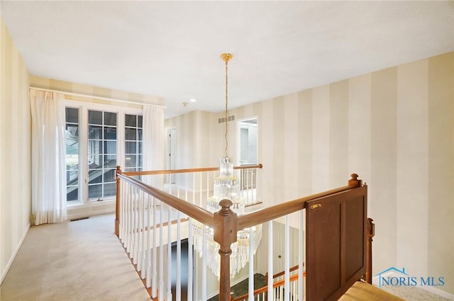 hallway with an inviting chandelier and light colored carpet