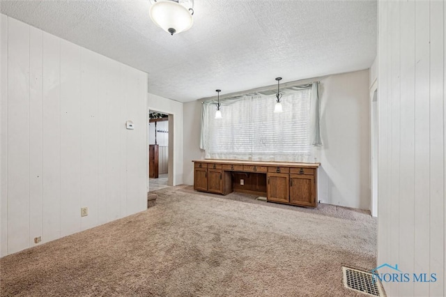 spare room with built in desk, light carpet, and a textured ceiling