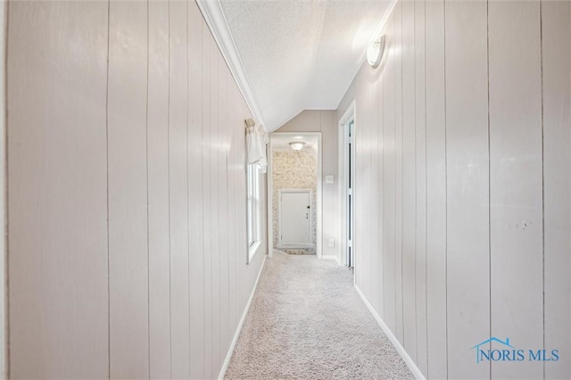 corridor with carpet flooring, vaulted ceiling, a textured ceiling, and wood walls