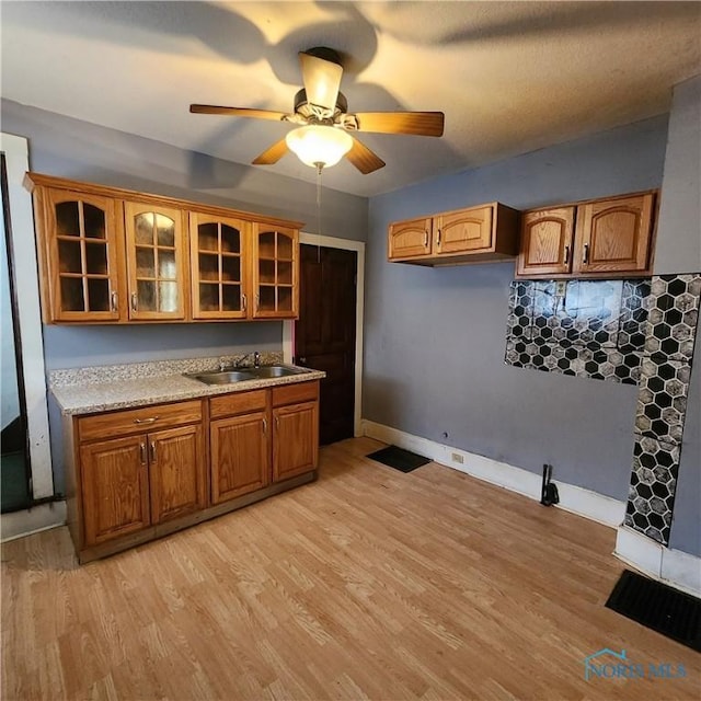 kitchen with ceiling fan, sink, light stone counters, and light hardwood / wood-style floors