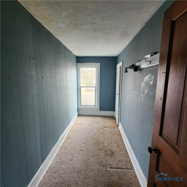 corridor with light colored carpet, wooden walls, and a textured ceiling