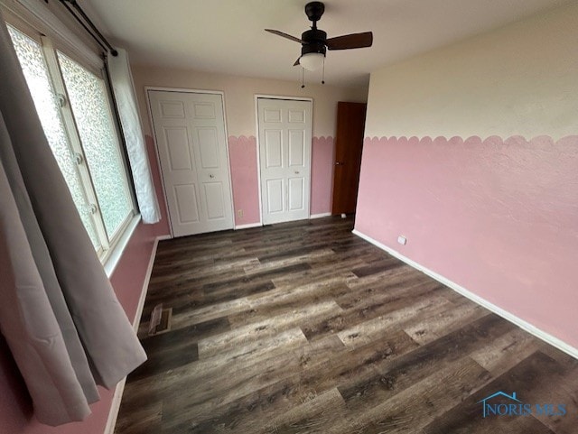 unfurnished bedroom with ceiling fan, dark hardwood / wood-style floors, and multiple windows