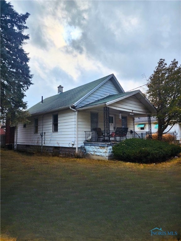 view of front of property featuring roof with shingles, a chimney, a porch, and a front yard