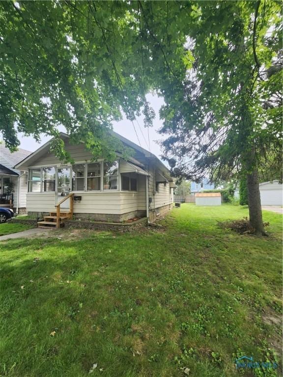 view of front of home featuring a sunroom, a shed, an outdoor structure, and a front yard