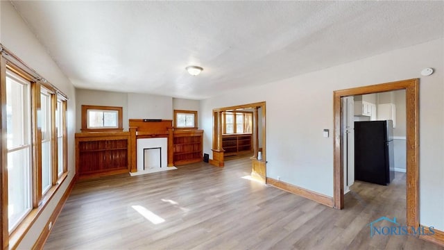 unfurnished living room with a healthy amount of sunlight, a textured ceiling, and light hardwood / wood-style flooring