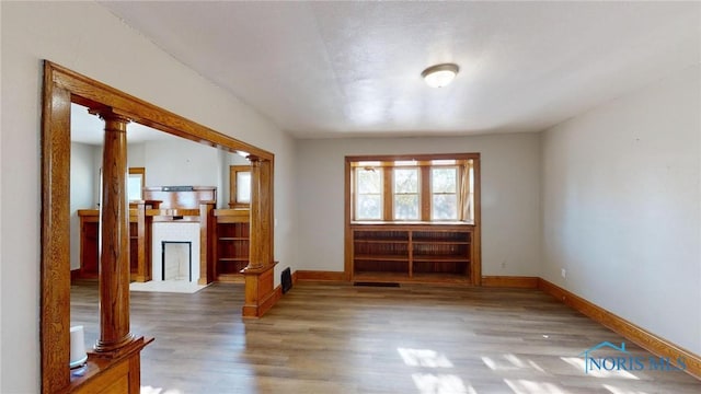 unfurnished room featuring a tiled fireplace, hardwood / wood-style floors, and ornate columns