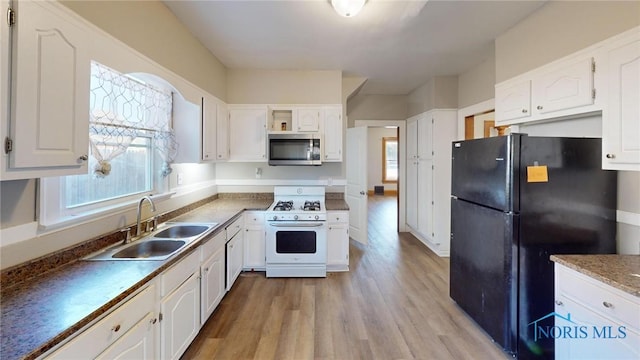 kitchen with black refrigerator, white gas range, white cabinetry, and sink