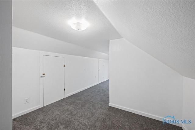 bonus room featuring lofted ceiling, dark carpet, and a textured ceiling