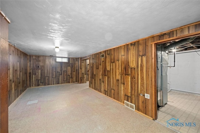 basement featuring wooden walls and a textured ceiling