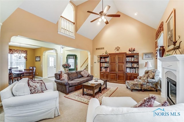 carpeted living room with ceiling fan with notable chandelier and high vaulted ceiling