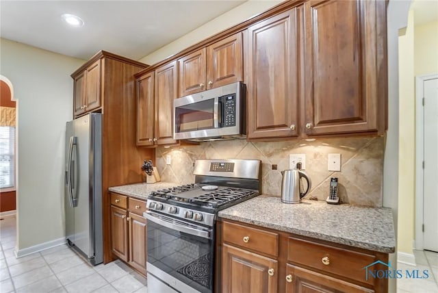 kitchen with light stone counters, light tile patterned floors, decorative backsplash, and stainless steel appliances