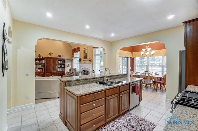 kitchen with sink, appliances with stainless steel finishes, light stone counters, an island with sink, and light tile patterned flooring