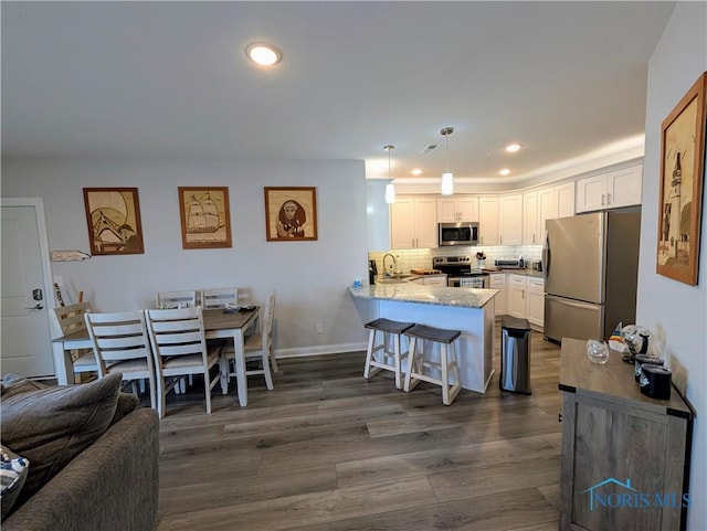 kitchen with a breakfast bar, kitchen peninsula, pendant lighting, stainless steel appliances, and white cabinets