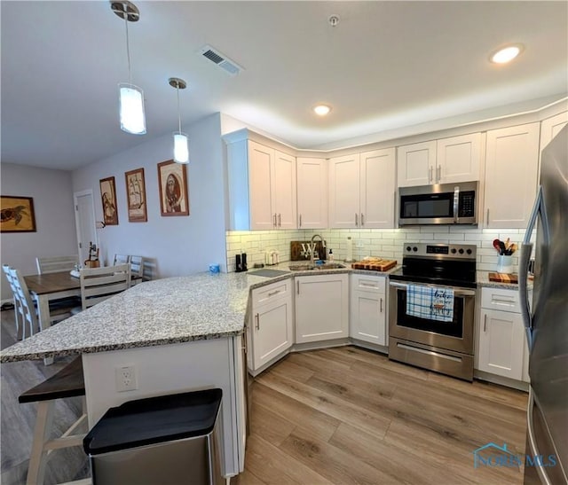 kitchen featuring sink, appliances with stainless steel finishes, white cabinets, decorative light fixtures, and kitchen peninsula