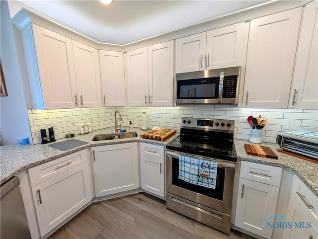 kitchen featuring sink, light stone counters, stainless steel appliances, light hardwood / wood-style floors, and white cabinets