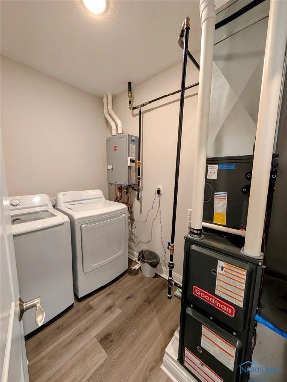 laundry area with water heater, heating unit, washer and clothes dryer, and light hardwood / wood-style flooring