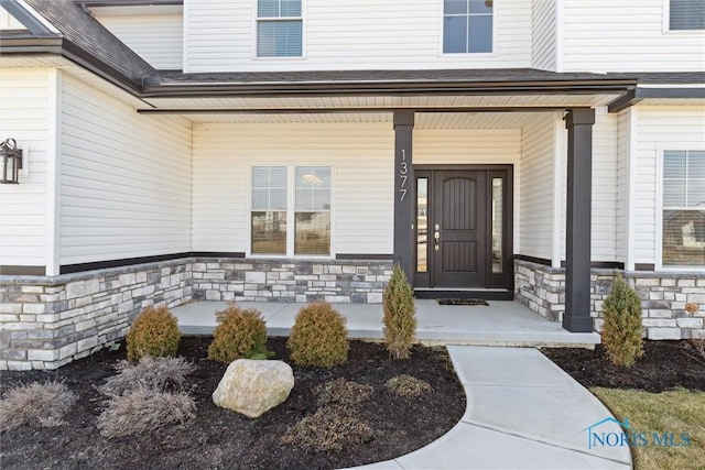 entrance to property with stone siding, a shingled roof, and a porch