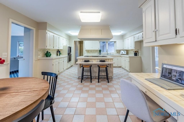 kitchen with white cabinetry, a breakfast bar area, island range hood, and tile counters