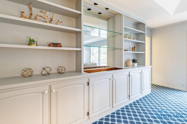 bar featuring a textured ceiling, ornamental molding, built in shelves, and white cabinets