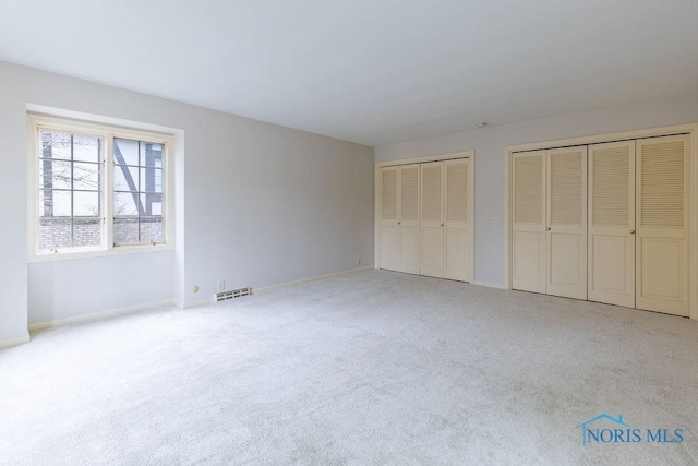 unfurnished bedroom with light colored carpet and multiple closets