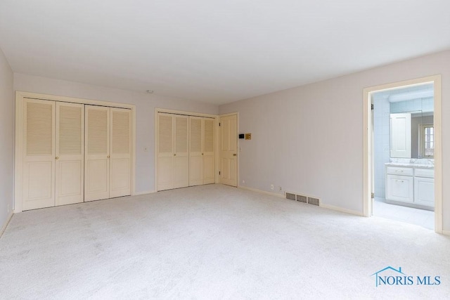 unfurnished bedroom with light carpet, ensuite bath, and multiple closets