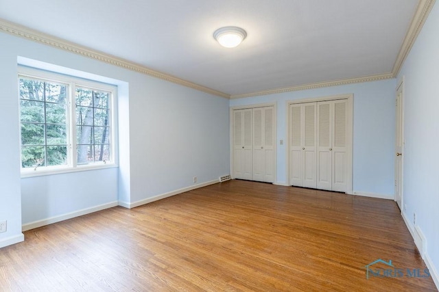 unfurnished bedroom with multiple closets, crown molding, and light wood-type flooring