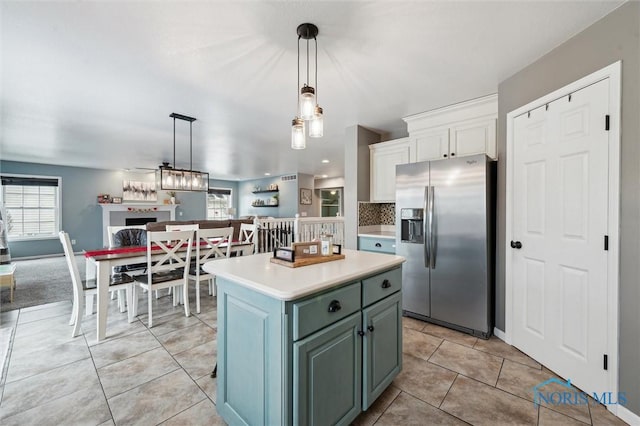 kitchen with pendant lighting, light tile patterned floors, stainless steel refrigerator with ice dispenser, white cabinets, and a kitchen island