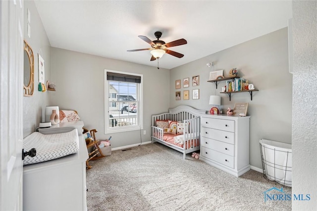 carpeted bedroom with a crib and ceiling fan