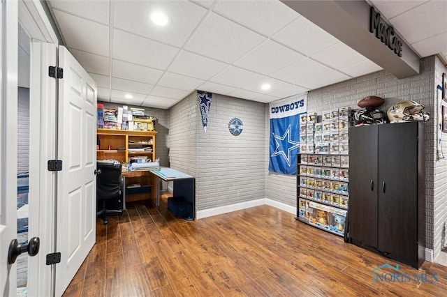 office space featuring brick wall, wood-type flooring, and a drop ceiling