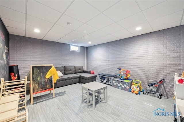 rec room featuring hardwood / wood-style flooring, brick wall, and a drop ceiling