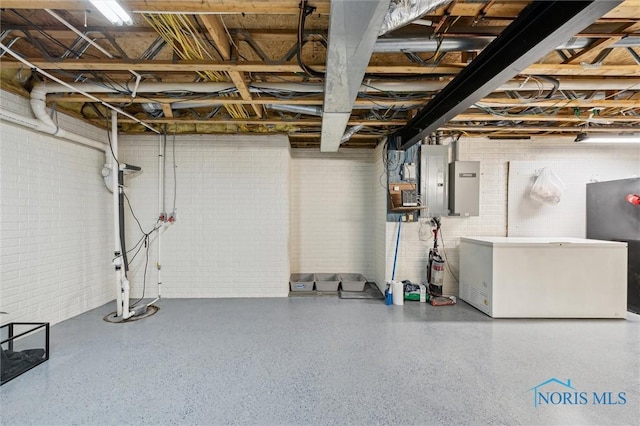 basement featuring brick wall, electric panel, and refrigerator