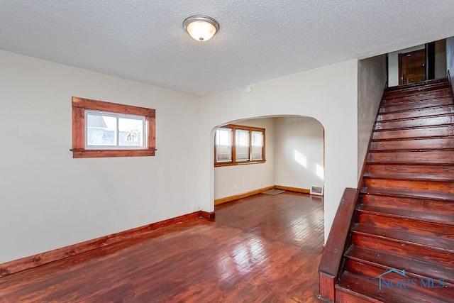 unfurnished room featuring a healthy amount of sunlight, a textured ceiling, and dark hardwood / wood-style flooring