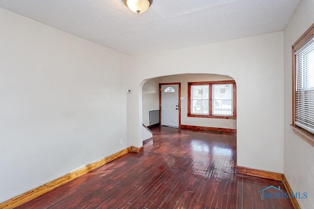 spare room featuring dark wood-type flooring, plenty of natural light, and a textured ceiling