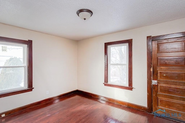 spare room with dark wood-type flooring, a textured ceiling, and a wealth of natural light