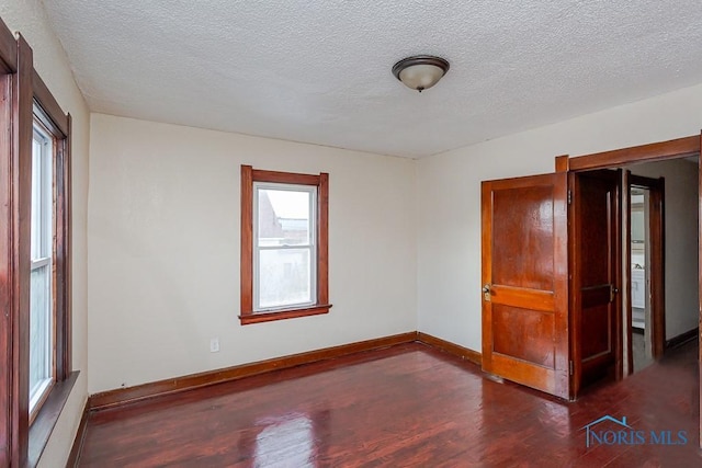 empty room with plenty of natural light, dark hardwood / wood-style floors, and a textured ceiling