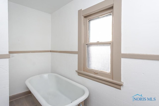 bathroom featuring hardwood / wood-style floors, tile walls, and a tub to relax in