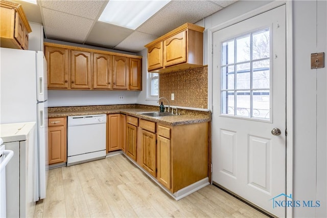 kitchen with white appliances, light wood-style flooring, brown cabinets, a paneled ceiling, and a sink