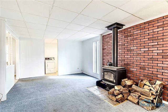 unfurnished living room with a wood stove, washer / dryer, carpet floors, and a paneled ceiling