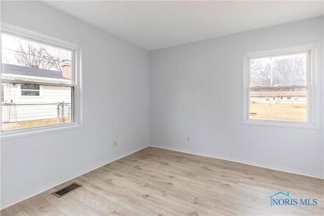 empty room featuring light wood finished floors, baseboards, and visible vents