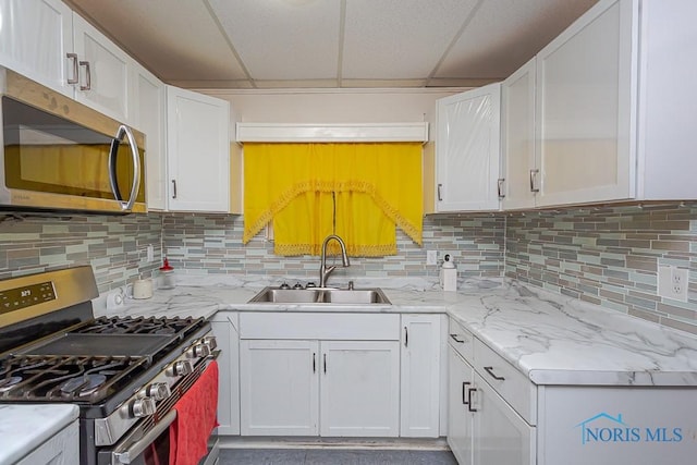 kitchen with a drop ceiling, appliances with stainless steel finishes, sink, and white cabinets