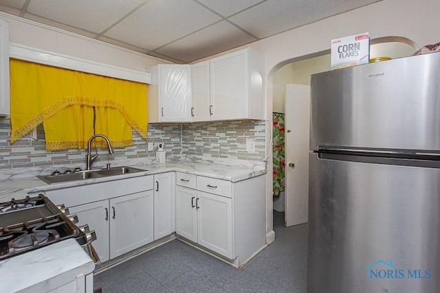 kitchen with sink, a paneled ceiling, appliances with stainless steel finishes, backsplash, and white cabinets