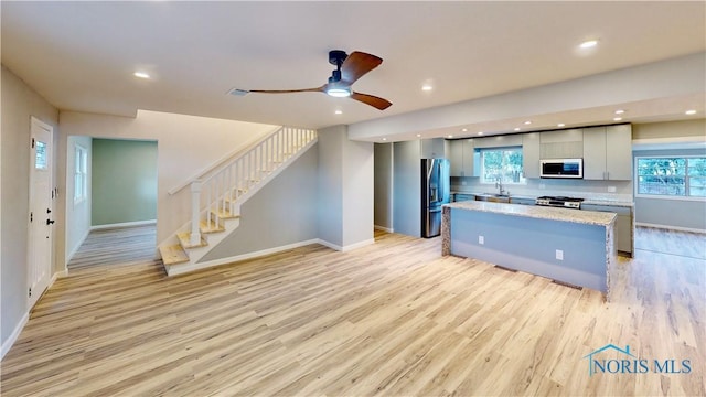 kitchen featuring light hardwood / wood-style flooring, stove, a center island, light stone counters, and stainless steel fridge with ice dispenser