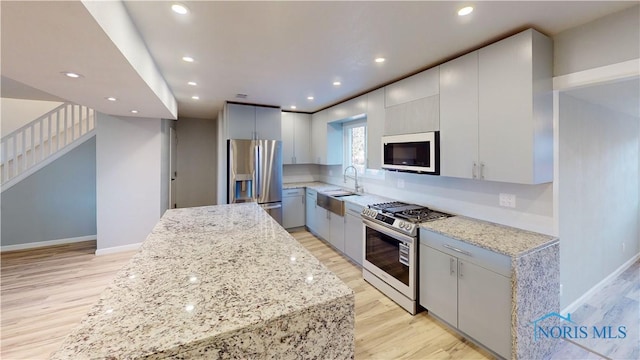 kitchen featuring sink, light wood-type flooring, light stone countertops, and appliances with stainless steel finishes