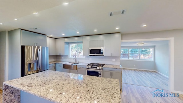 kitchen with stainless steel appliances, a kitchen island, sink, and light stone counters