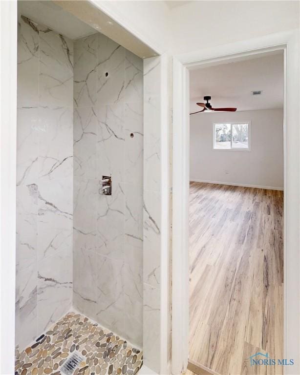 bathroom featuring ceiling fan, wood-type flooring, and tiled shower