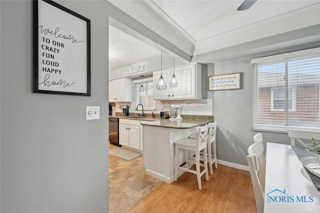 kitchen featuring sink, a breakfast bar area, dishwasher, white cabinetry, and decorative light fixtures