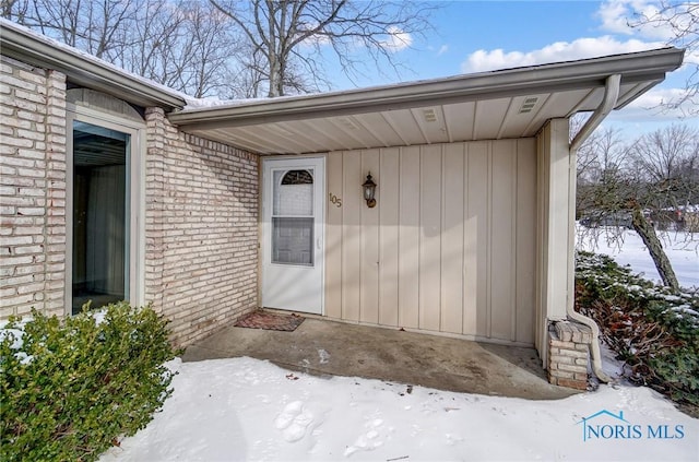 snow covered property entrance with brick siding