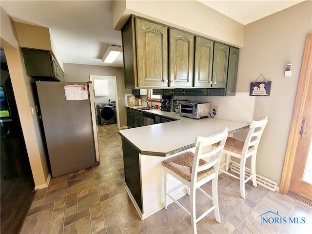 kitchen with washer / dryer, sink, appliances with stainless steel finishes, kitchen peninsula, and green cabinets