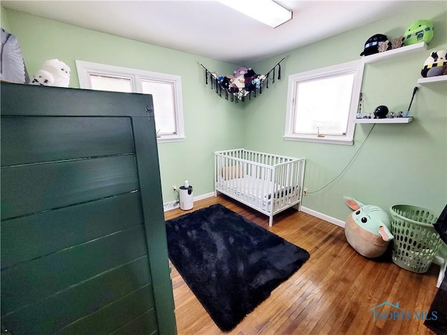 bedroom with multiple windows, a nursery area, and hardwood / wood-style flooring